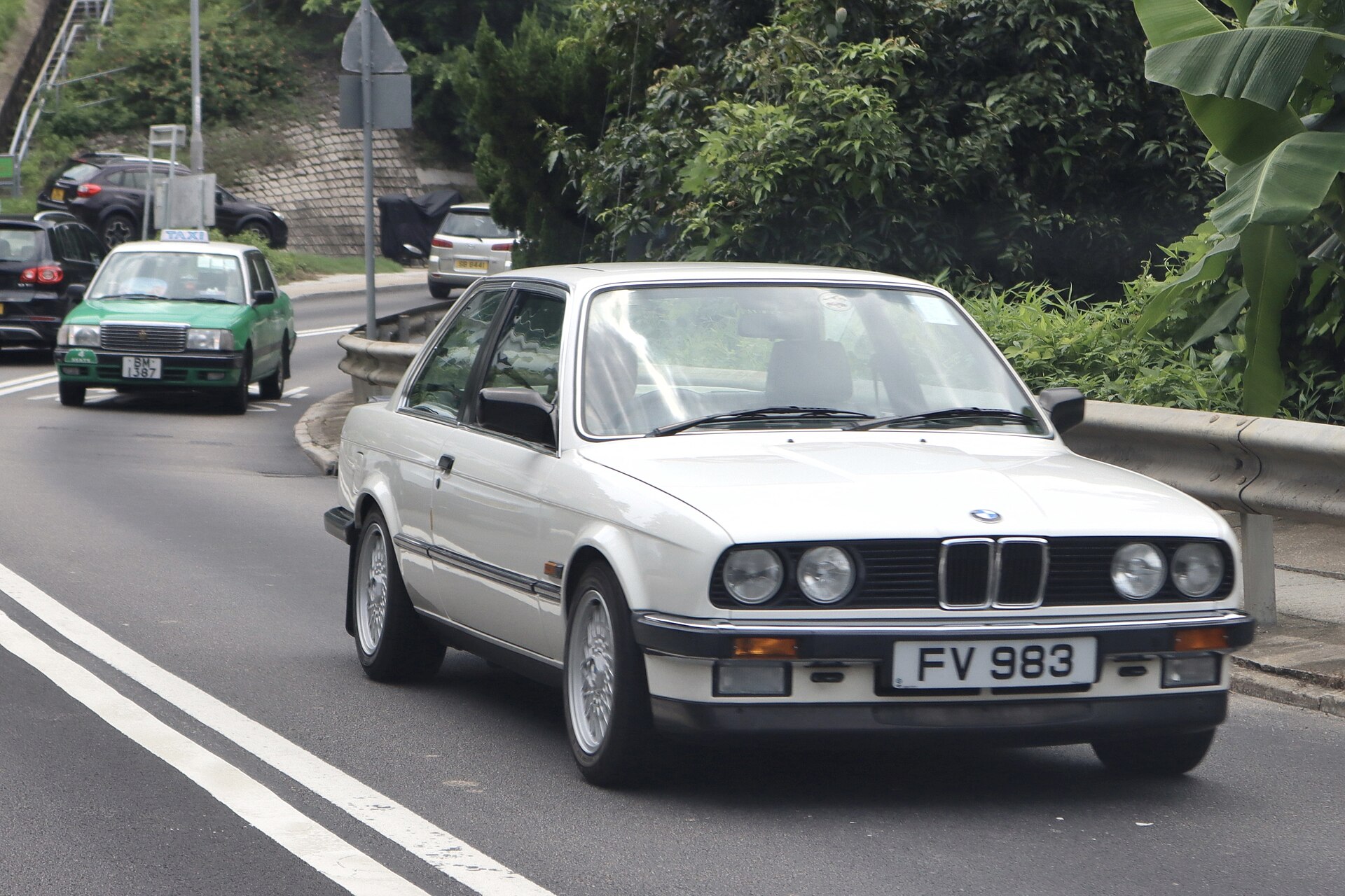 White two-door BMW E30 sedan photographed driving on a public road