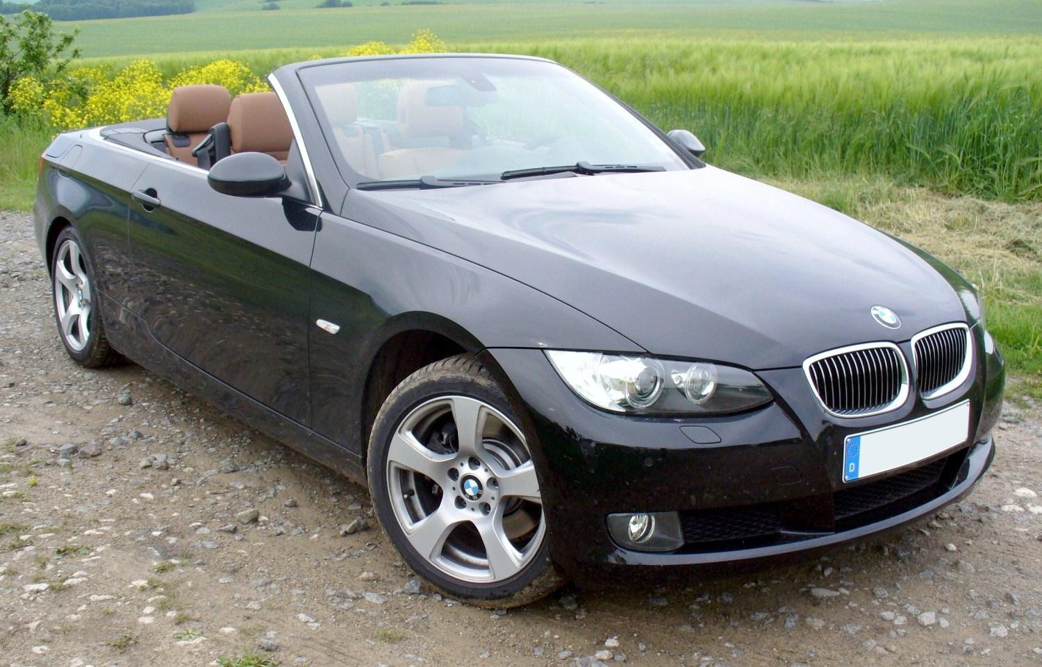 Black BMW E93 Cabriolet with its roof open beside a green field